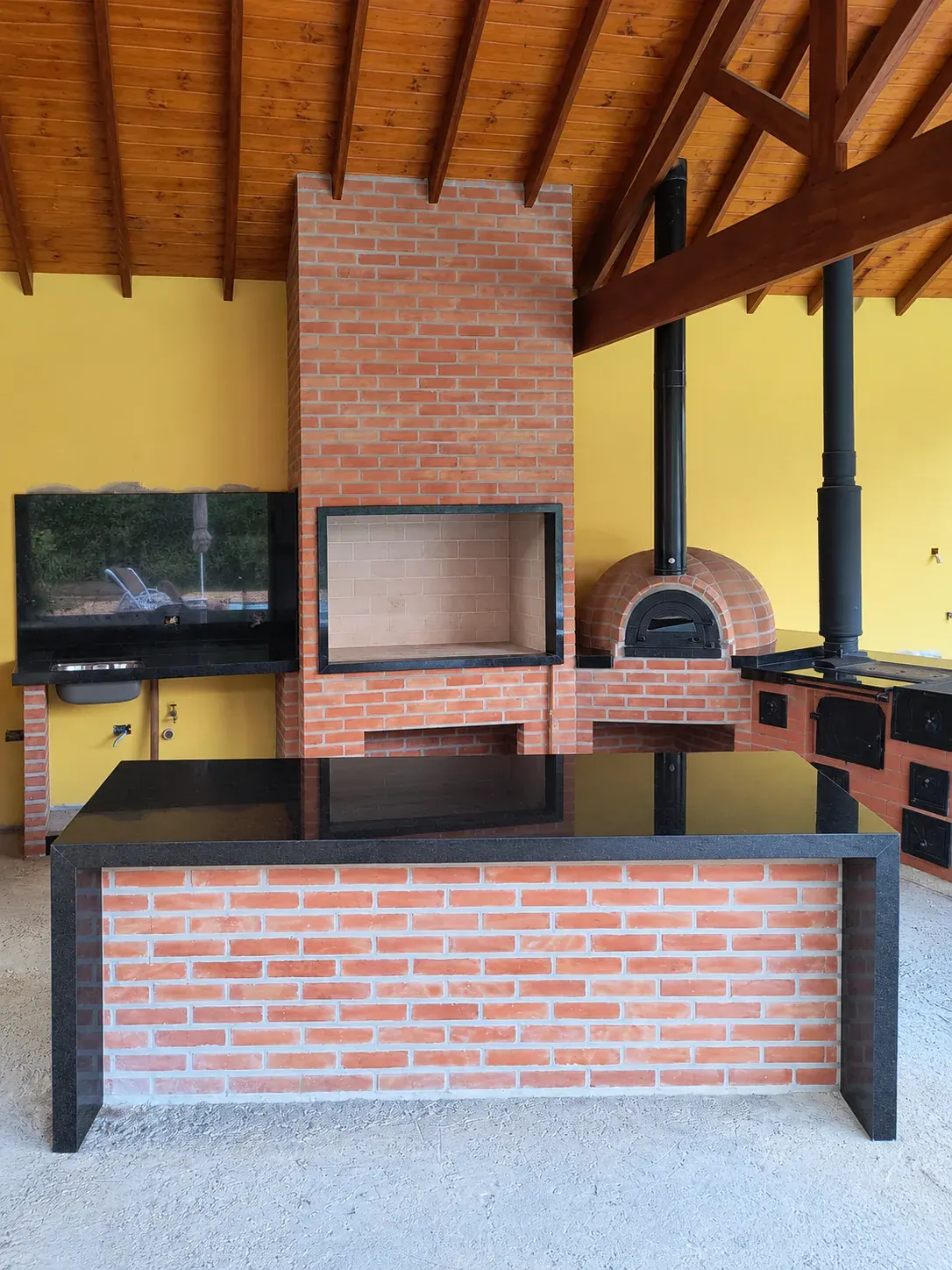 Área gourmet coberta com churrasqueira de tijolos, forno igloo (pizza) e fogão a lenha.