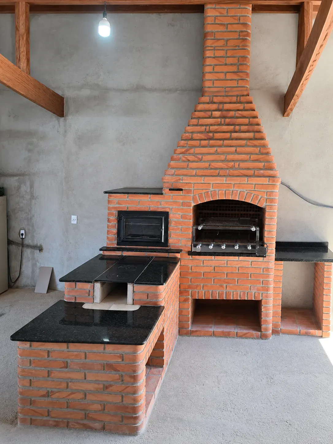 Churrasqueira de tijolos com fogão a lenha de duas bocas e forno lateral.