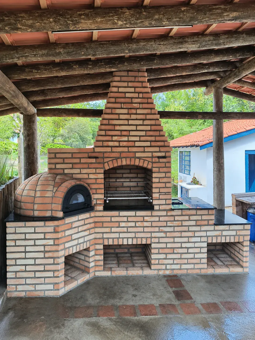Churrasqueira de tijolos com forno igloo (pizza) sob cobertura de madeira.